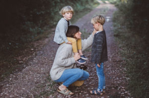Mutter mit Sohn auf den Schultern kniet sich zu ihrem zweiten Sohn um ihn zu trösten bei Familienfotoshooting Freiburg