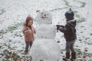 Kinder im Schneegestöber mit Schneemann bei Familienfotoshooting Freiburg