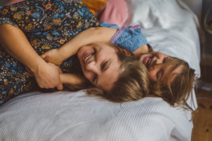 Mutter tobt mit Tochter auf dem Bett bei Schwangerschafts Fotoshooting Basel