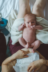 Ein Neugeborenes auf dem Schoß seiner Mutter im Wochenbett bei einem Neugeborenenfotoshooting in Freiburg