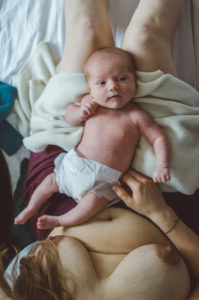 Ein Neugeborenes in Windel auf dem Bauch seiner Mutter bei einem Neugeborenenfotoshooting in Freiburg