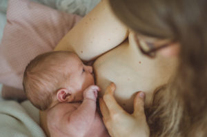 Mutter stillt ihr Neugeborenes im Wochenbett bei fotoshooting Zuhause in Freiburg