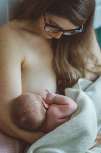 Eine Mutter stillt ihr Neugeborenes im Wochenbett bei einem Neugeborenenfotoshooting in Freiburg