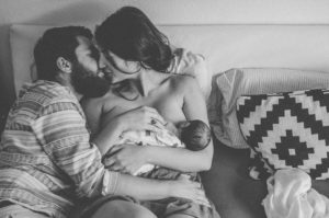 Vater und Mutter küssen sich mit ihrem Neugeborenen Säugling im Wochenbett entstanden bei Neugeborenenfotoshooting in Freiburg