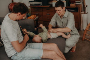 Eine Mutter wickelt ihr Baby mit Stoffwindeln während der Vater mit ihm spielt bei dokumentarischem Familienfotoshooting in Freiburg