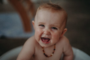 Lachendes Babyfoto mit Bernsteinkette von Kinderfotograf in Freiburg