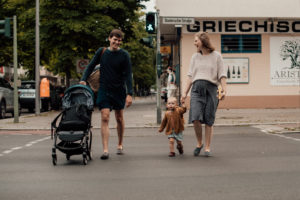 Eine Familie mit Kleinkind und Babybauch überquert lachend eine Straße entstanden bei einem Familienfotoshooting