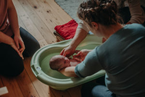 Foto einer Mutter mit Neugeborenen beim ersten Babybad nach der Geburt mit der Hebamme entstanden bei einem Fotoshooting Zuhause im Wochenbett bei Freiburg