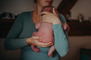 Foto eines Neugeborenen Baby auf dem Arm seiner Mutter entstanden bei einem Neugeborenenfotoshooting Zuhause bei Freiburg