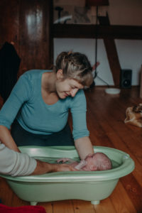 Foto einer Mutter mit Neugeborenen beim ersten Babybad nach der Geburt entstanden bei einem Fotoshooting Zuhause im Wochenbett bei Freiburg