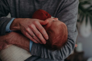 Neugeborenenfoto von Papas Hand die das Köpfchen vom Baby hält entstanden bei Babyfotoshooting Zuhause in Freiburg
