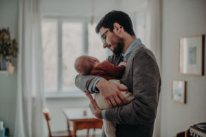 Neugeborenenfoto von Vater mit seinem Baby auf dem Arm entstanden bei Babyfotoshooting Zuhause in Freiburg