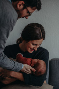 Neugeborenenfoto von Vater mit Baby und Mutter entstanden bei Babyfotoshooting Zuhause in Freiburg