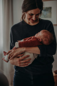 Natürliches Neugeborenenfoto von Baby entstanden im Arm der Mutter bei Babyfotoshooting Zuhause in Freiburg