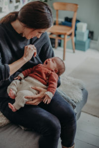 Natürliches Neugeborenenfoto von gähnendem Baby im Arm der Mutter entstanden bei einem Babyfotoshooting Zuhause im Wochenbett in Freiburg