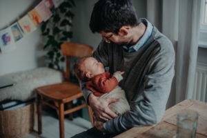 Natürliches Neugeborenenfoto von Baby auf Papas Arm entstanden bei einem Babyfotoshooting Zuhause im Wochenbett in Freiburg