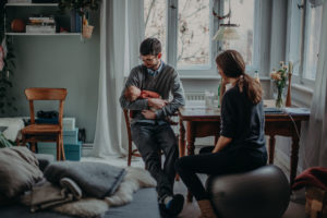 Natürliches Familienfoto von Baby auf Papas Arm entstanden bei einem Babyfotoshooting Zuhause im Wochenbett in Freiburg
