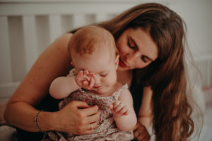Müdes Baby reibt sich Augen auf dem Arm der Mutter, natürliches Familienfoto entstanden bei Familienfotoshooting in Freiburg