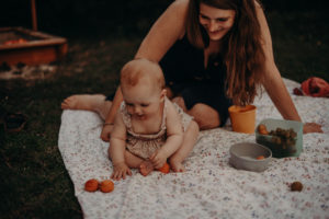 Mutter mit Baby auf Picknickdeke im Garten, natürliches Familienfoto entstanden bei Familienfotoshooting in Freiburg