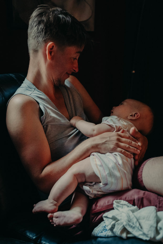 Stockfotos lgbtqia+ ein Trans Vater lächelt sein Baby an beim stillen
