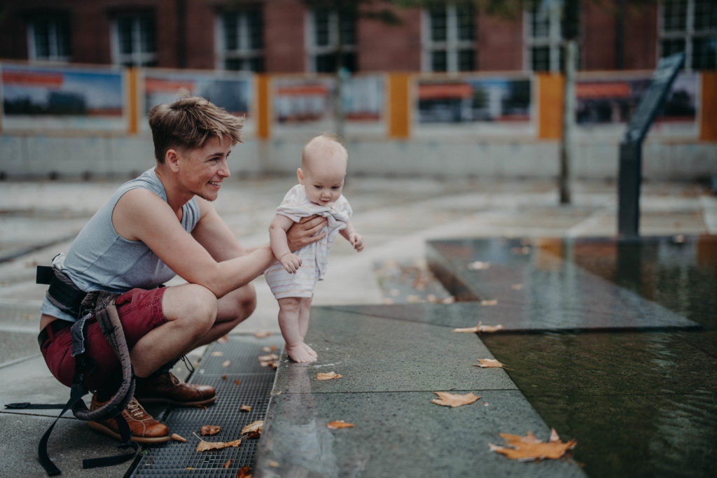 Stockfotos lgbtqia+ Trans Vater mit Kind und Babytrage am Wasser